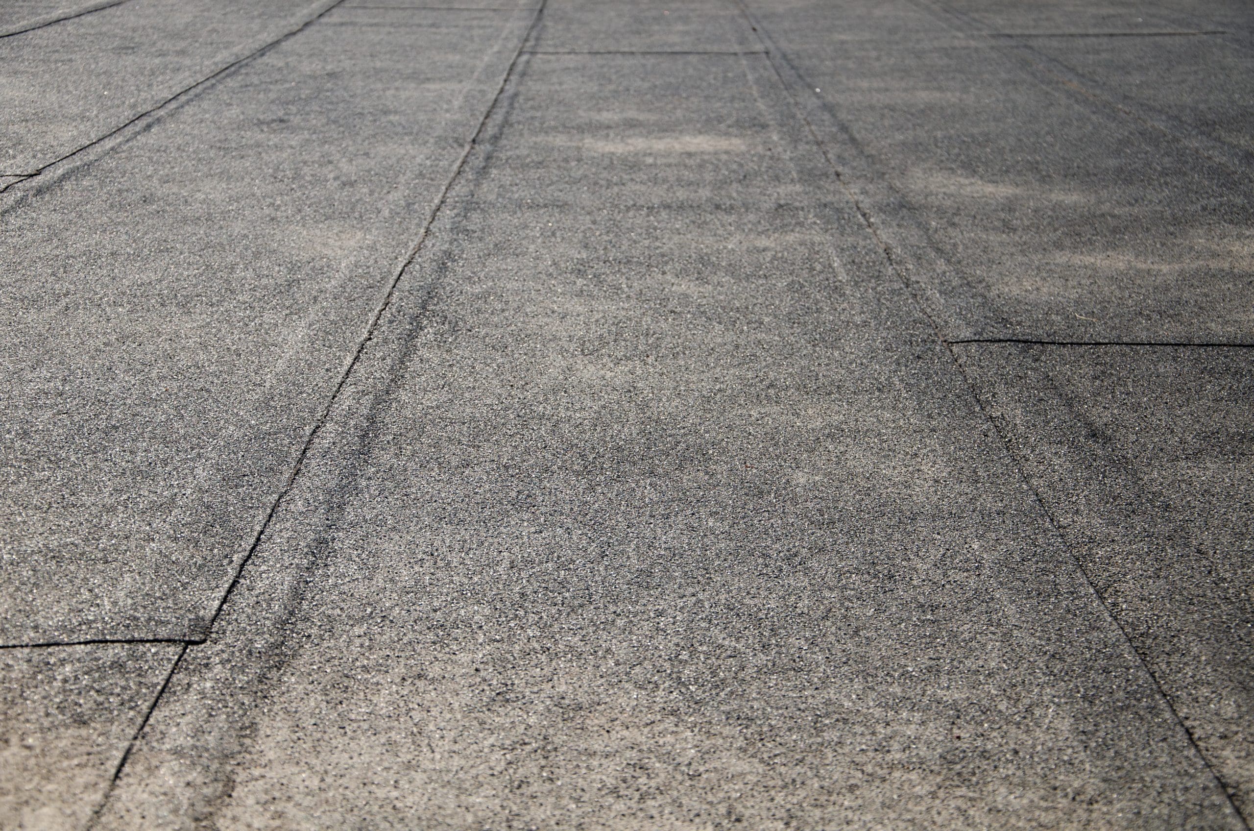 Close-up view of a flat, textured surface with subtle lines and seams, suggesting a rooftop or paved area. The surface appears to be made of asphalt or a similar material, with a gray, slightly rough texture.